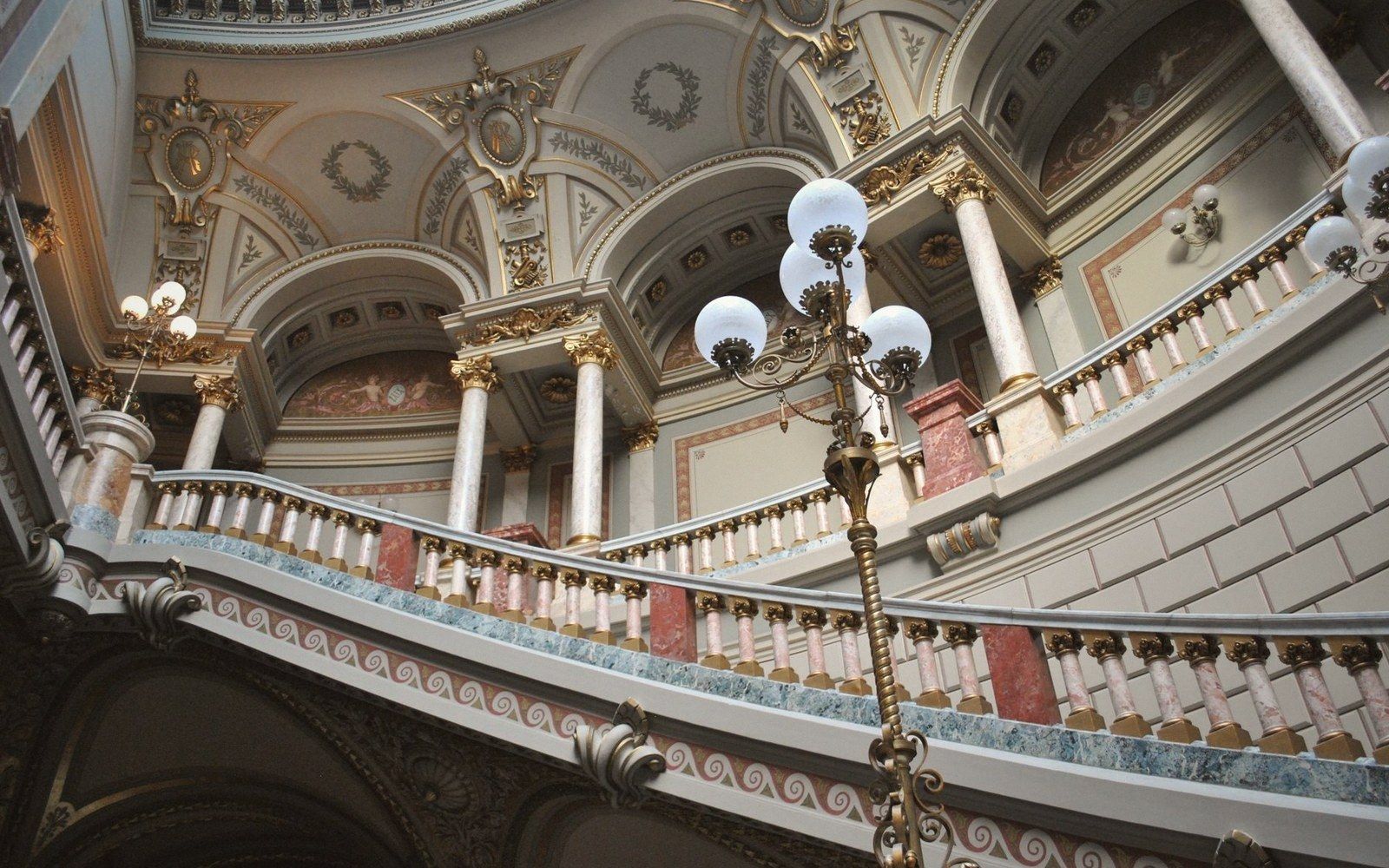 A grand museum staircase with marble balustrades and a painted ceiling, seen from below